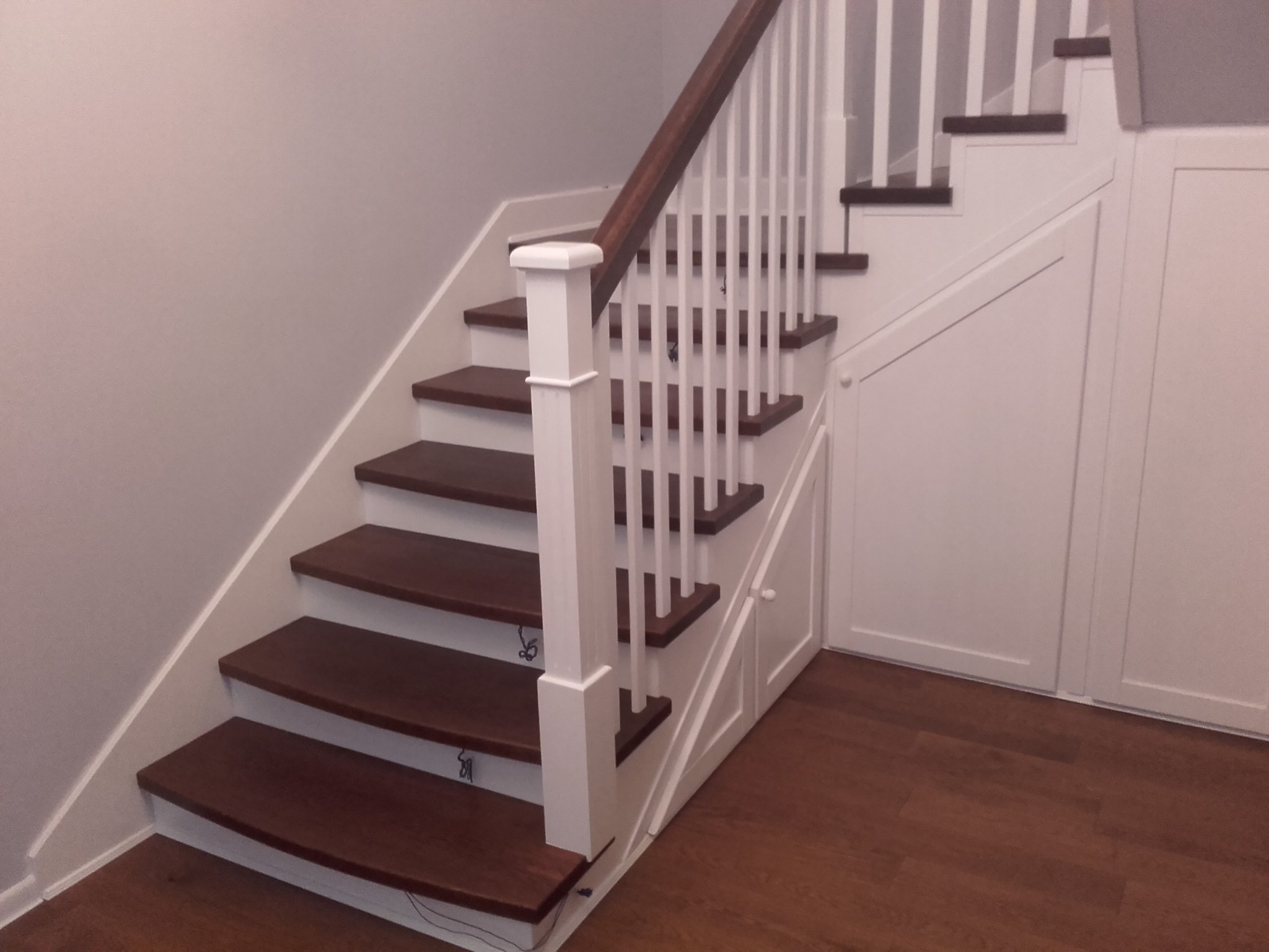 Schody drewniane z białymi balustradami i zabudową pod schodami, widok z dołu, oświetlenie mieszane.