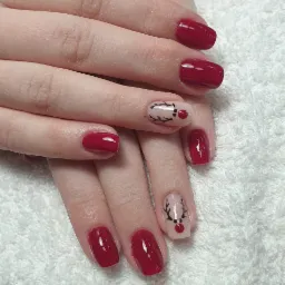 Dłonie z czerwonymi paznokciami i świątecznym zdobieniem renifera na dwóch paznokciach, ułożone na białym ręczniku.