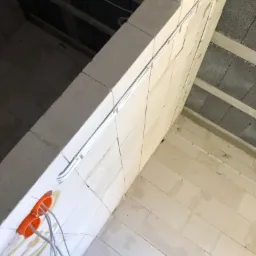 Surowe wnętrze w trakcie prac: widoczne przewody w peszlach mocowanych do ściany z betonu komórkowego, pomarańczowa puszka elektryczna z wyprowadzonymi kablami, sufit z szarego betonu.