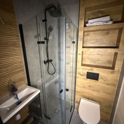 ProDremont Dmytro Nimenko - Nowoczesna łazienka z kabiną prysznicową typu walk-in, umywalką nablatową i podwieszaną toaletą. Drewniane panele ścienne z wnękami dodają ciepła szarej kolorystyce.