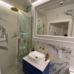 ProDremont Dmytro Nimenko - Elegancka łazienka z kabiną prysznicową w złotej ramie, umywalką nablatową na granatowej szafce i lustrem w białej ramie na tle marmurowych płytek.
