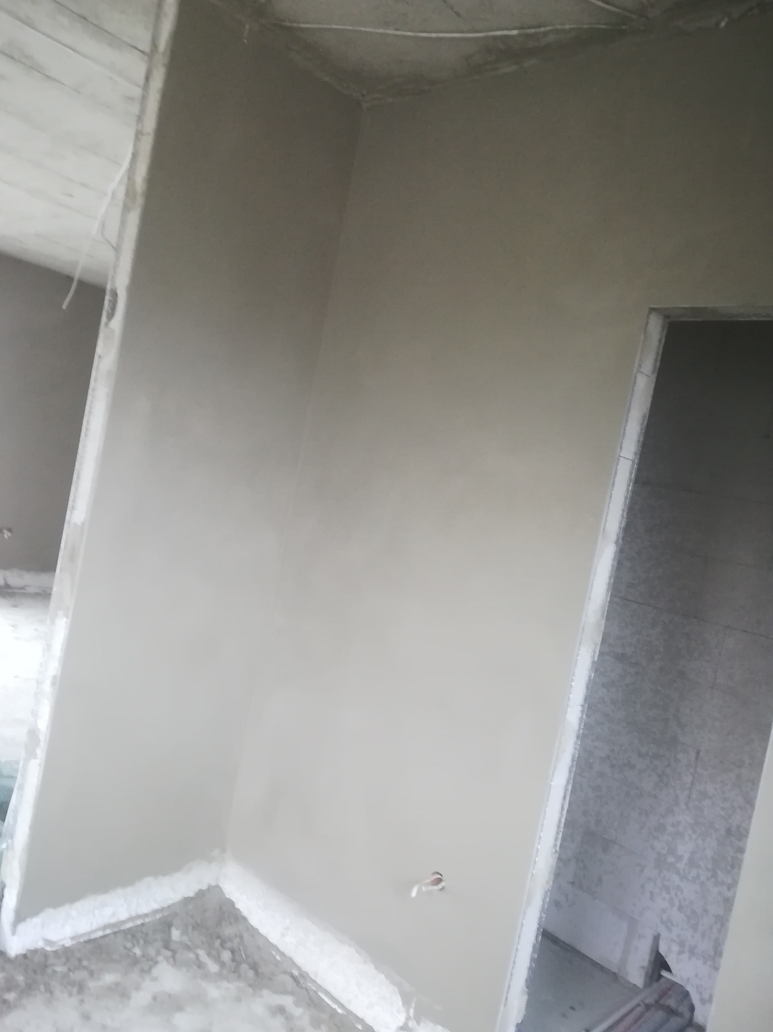Świeżo otynkowany narożnik pokoju w Lublinie, widoczne ślady po szpachlowaniu na podłodze i niedokończone obramowanie drzwi.