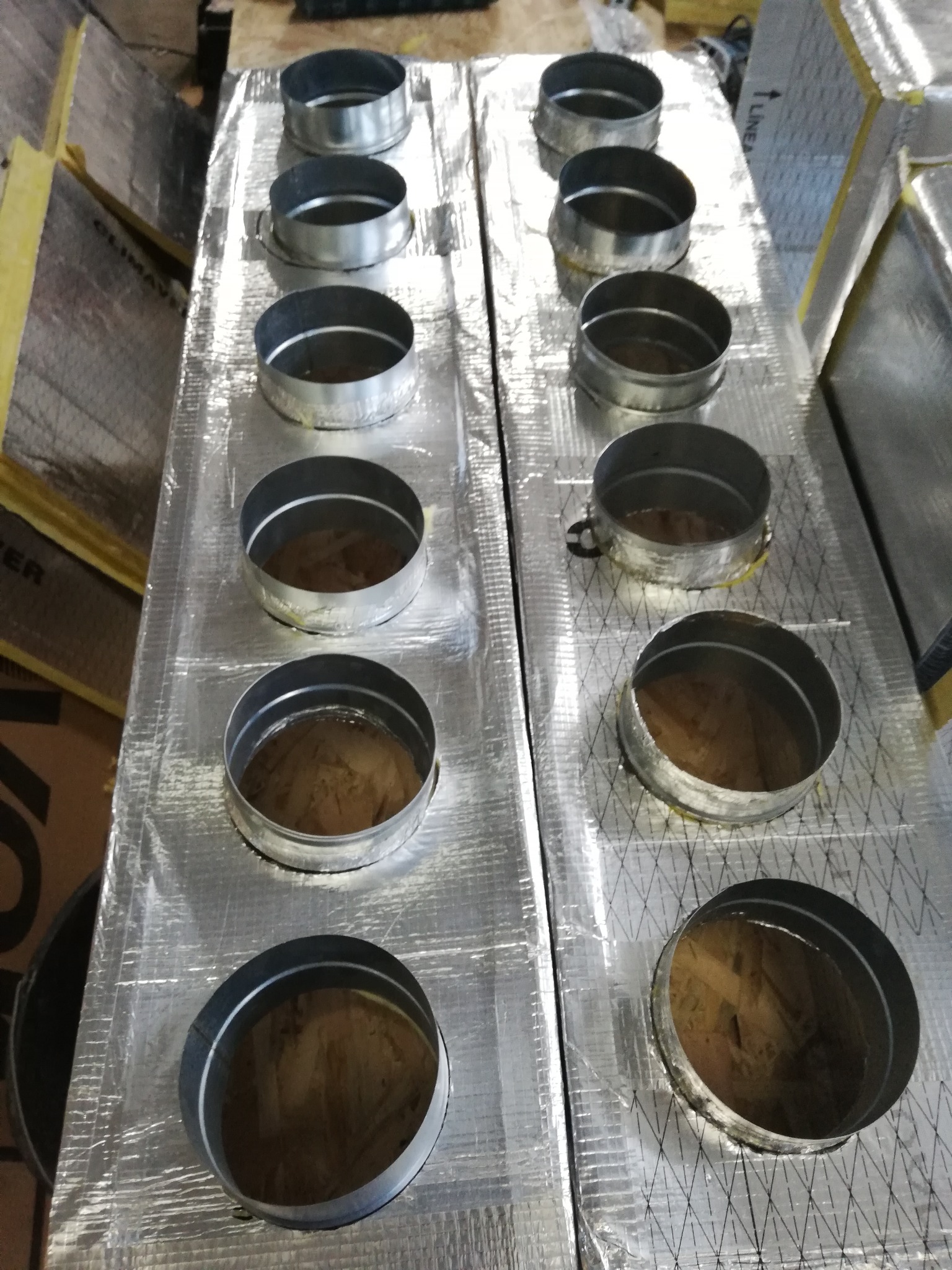 Dwa panele izolacyjne z otworami na metalowe kołnierze do podłączenia przewodów wentylacyjnych, przygotowane do montażu.