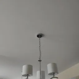 Biały sufit z zamontowaną, nowoczesną, chromowaną lampą wiszącą z trzema abażurami, widok z dołu.