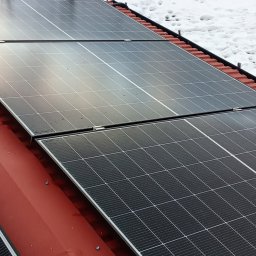 SES Group Fotowoltaika, Pompy Ciepła, Kotły, Klimatyzacja, Rekuperacja, Termomodernizacja - Panele słoneczne na czerwonym dachu w zimowej scenerii. Widoczne ślady śniegu. Ujęcie z góry, podkreślające regularny układ paneli i kontrast kolorów.
