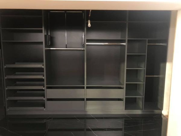 Wnętrze dużej, grafitowej garderoby z szufladami i półkami, widoczne relingi na ubrania, marmurowa posadzka.