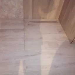 Ukończona podłoga w łazience wyłożona panelami podłogowymi imitującymi drewno, z wbudowanym odpływem liniowym.