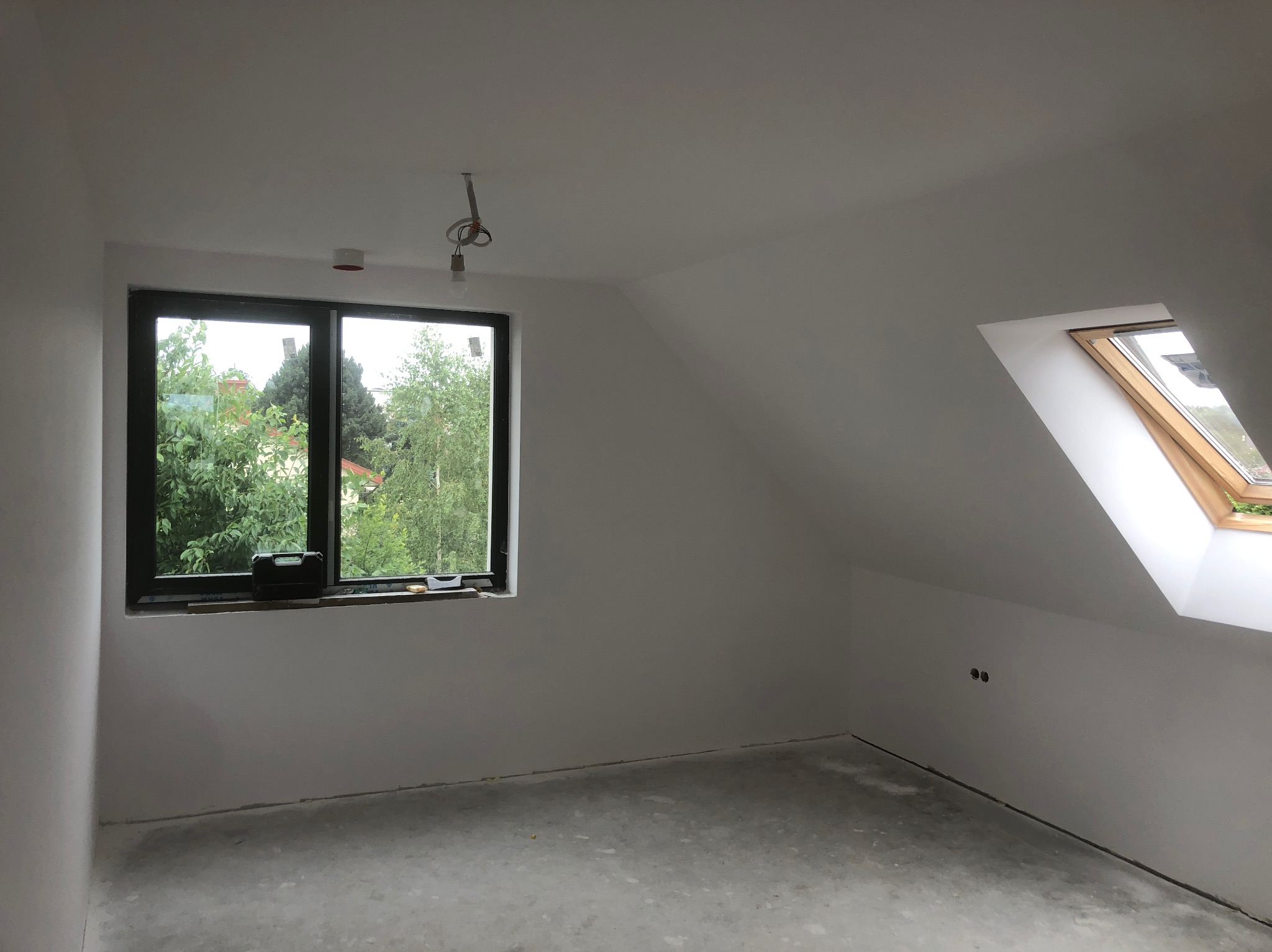 Poddasze po szpachlowaniu i gładziowaniu, z oknem dachowym i poziomym, przygotowane do malowania, widoczne narzędzia na parapecie.