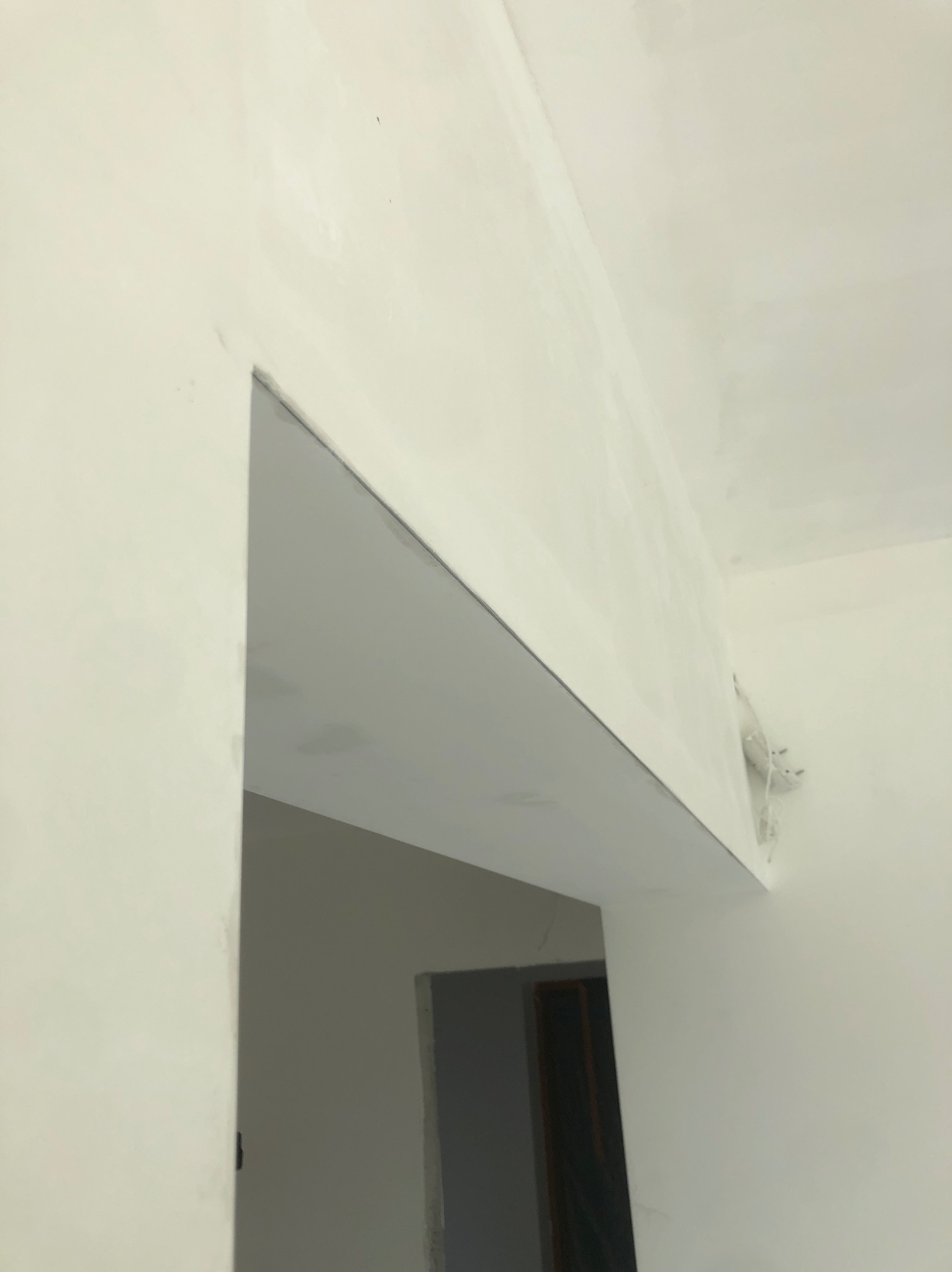 Niedokończona ściana i sufit po nałożeniu warstwy szpachli, widoczne nierówności i niedociągnięcia, fragment instalacji elektrycznej wystający ze ściany.