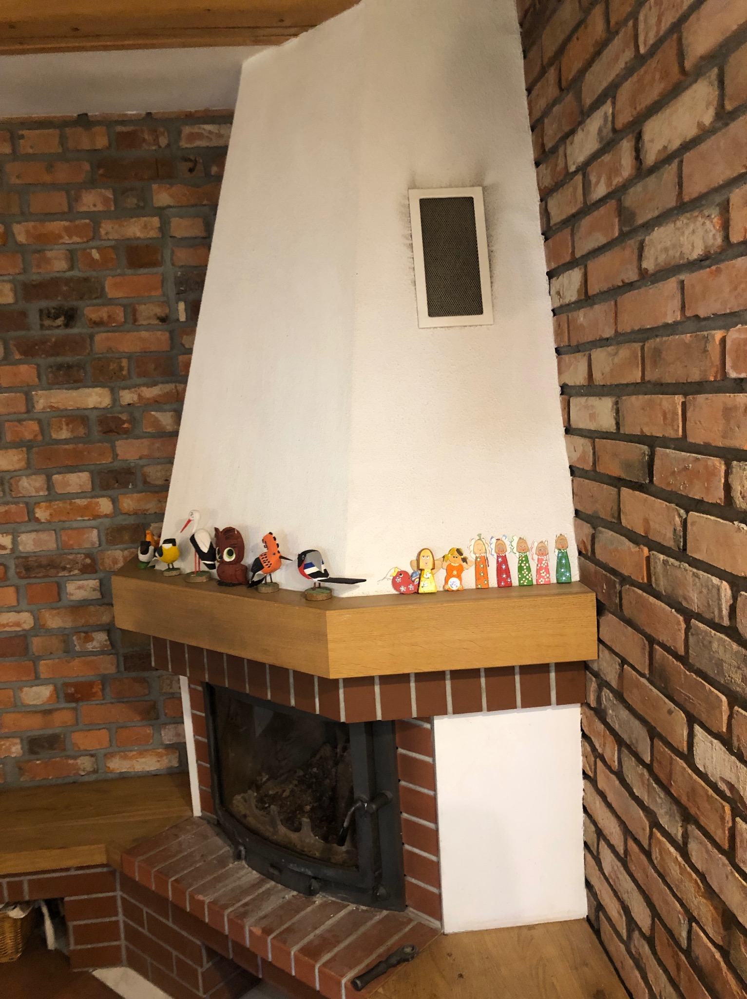 Otynkowany komin z ceglaną obudową, drewnianym blatem i kolekcją drewnianych figurek ptaków i aniołów.