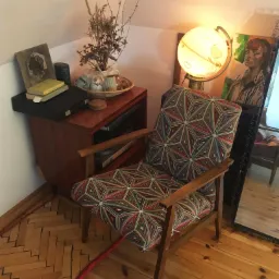 Fotel z geometrycznym wzorem obok lampy w kształcie globu i lustra w pokoju na poddaszu.