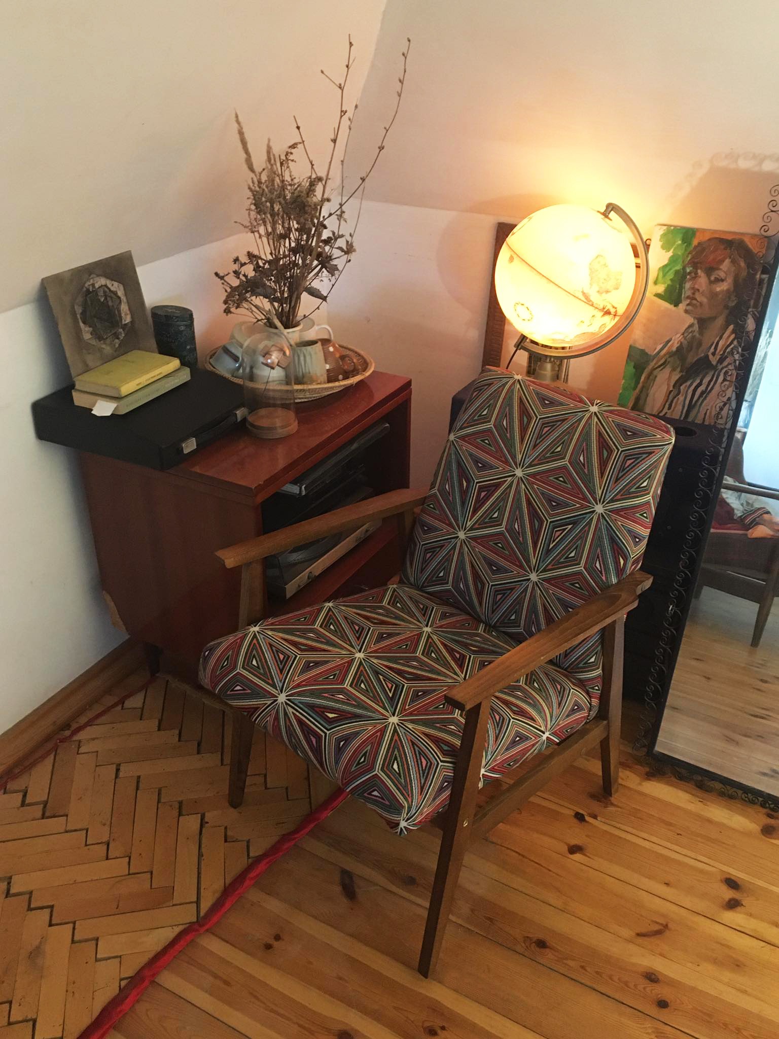 Fotel z geometrycznym wzorem obok lampy w kształcie globu i lustra w pokoju na poddaszu.