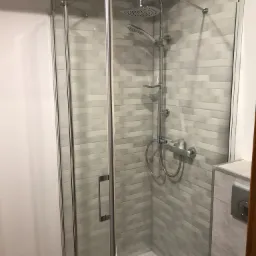 Szklana kabina prysznicowa z deszczownicą i baterią termostatyczną, wykończona szarymi płytkami imitującymi cegłę.