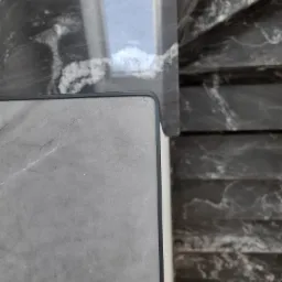 Fragment marmurowych schod&oacute;w z szarymi stopniami i ciemniejszymi podstopnicami, widoczne z g&oacute;ry, z fragmentem barierki z szarego marmuru z czarnym wykończeniem.