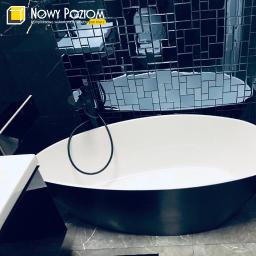 Nowy Poziom - Nowoczesna, owalna wanna wolnostojąca w łazience z czarną mozaiką na ścianie i czarną armaturą.