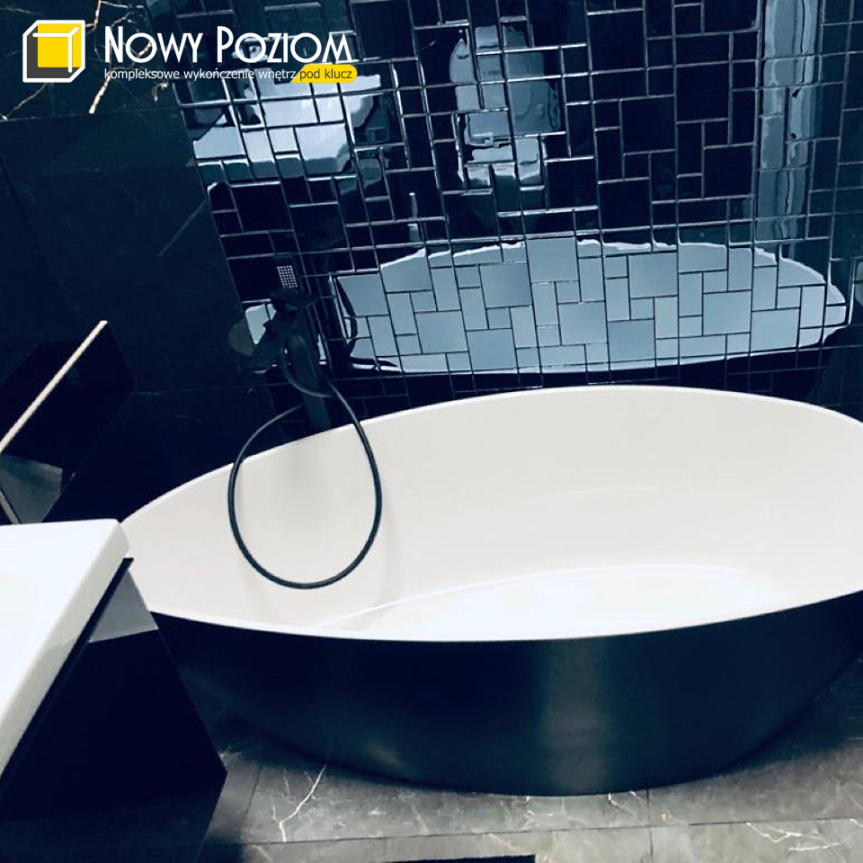 Nowoczesna, owalna wanna wolnostojąca w łazience z czarną mozaiką na ścianie i czarną armaturą.