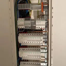 Otwarta skrzynka elektryczna z zainstalowanymi bezpiecznikami i przewodami, widoczne złącza i listwy montażowe, elementy marki Schneider Electric.