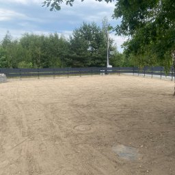 Zielono Mi - Wyrównany teren pod budowę ogrodzony czarnym płotem, z widocznym drzewem i stertą betonowych bloczków. W tle las i słup energetyczny.