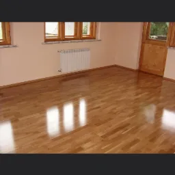 Błyszcząca podłoga z drewnianych desek w pustym pokoju z drewnianymi oknami i drzwiami, odbijająca światło.