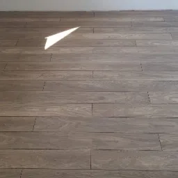 Ułożona podłoga z paneli imitujących drewno w jasnym, pustym pomieszczeniu, widoczny fragment białej ściany i odbicie światła na panelach.