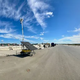 Mobilny system monitoringu z kamerami i panelem solarnym na placu budowy lotniska, błękitne niebo z chmurami w tle. Szeroki kadr, perspektywa.