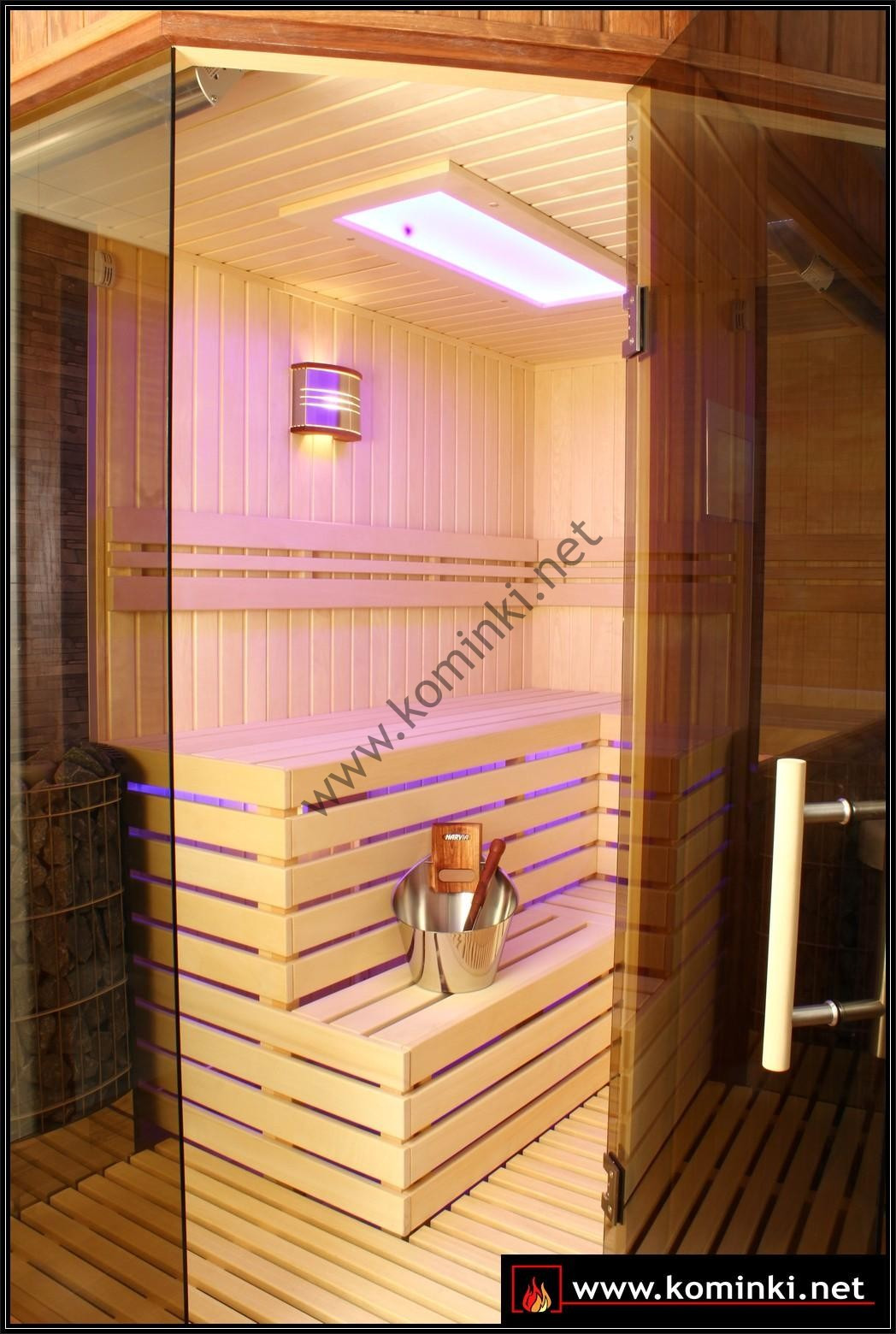 Wnętrze nowej sauny z jasnego drewna, z oświetleniem LED, szklanymi drzwiami i akcesoriami do sauny w metalowym wiaderku.