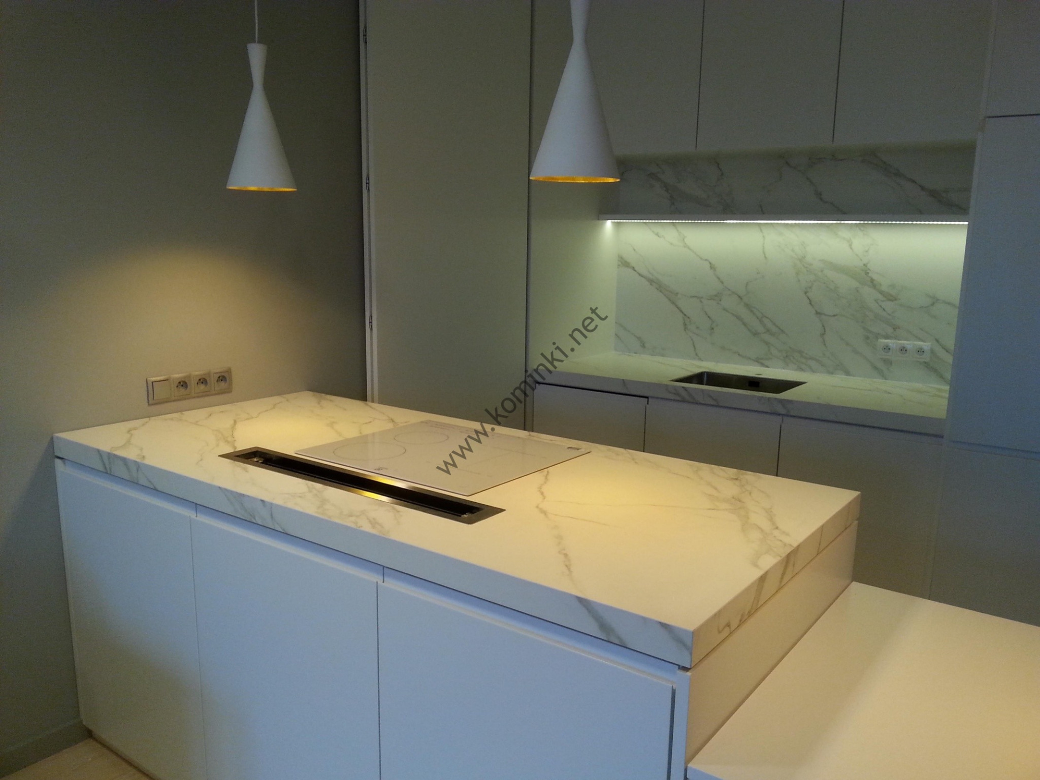 Nowoczesna kuchnia z wyspą i blatem z efektem marmuru, białe szafki, płyta indukcyjna zintegrowana z blatem i minimalistyczne lampy wiszące