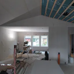 Wnętrze w trakcie montażu płyt kartonowo-gipsowych w Rypinie, widoczne stelaże sufitowe z izolacją, narzędzia do cięcia płyt oraz fragmenty instalacji elektrycznej.