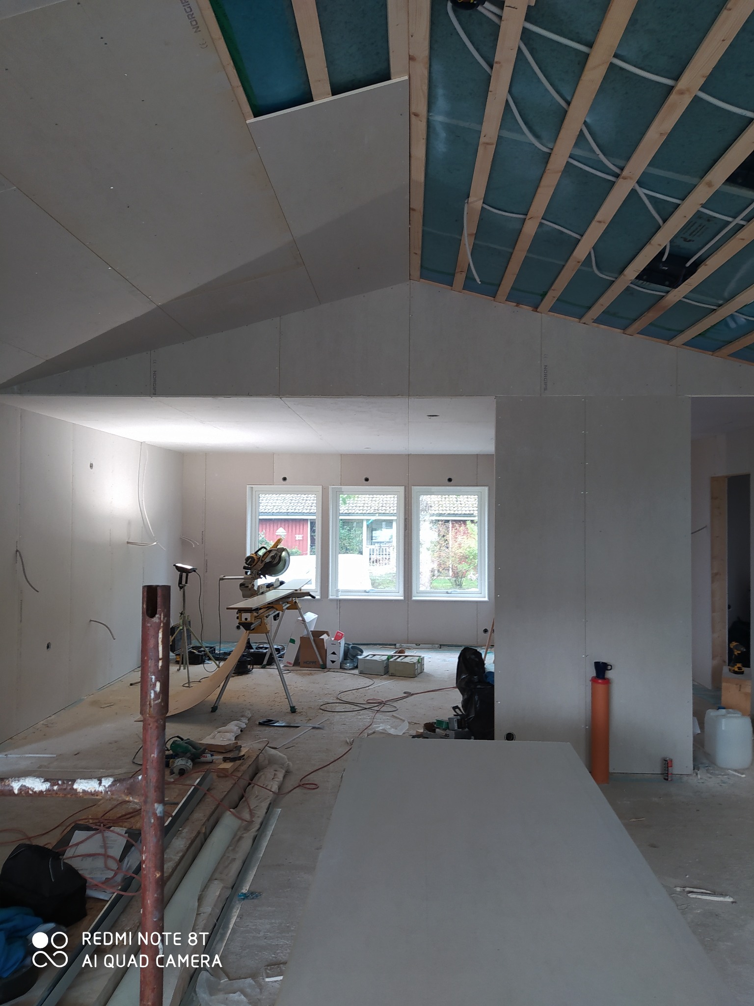 Wnętrze w trakcie montażu płyt kartonowo-gipsowych w Rypinie, widoczne stelaże sufitowe z izolacją, narzędzia do cięcia płyt oraz fragmenty instalacji elektrycznej.