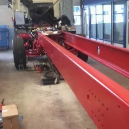 Czerwona rama ciężarówki na koziołkach w warsztacie, widoczne elementy podwozia i kabina.