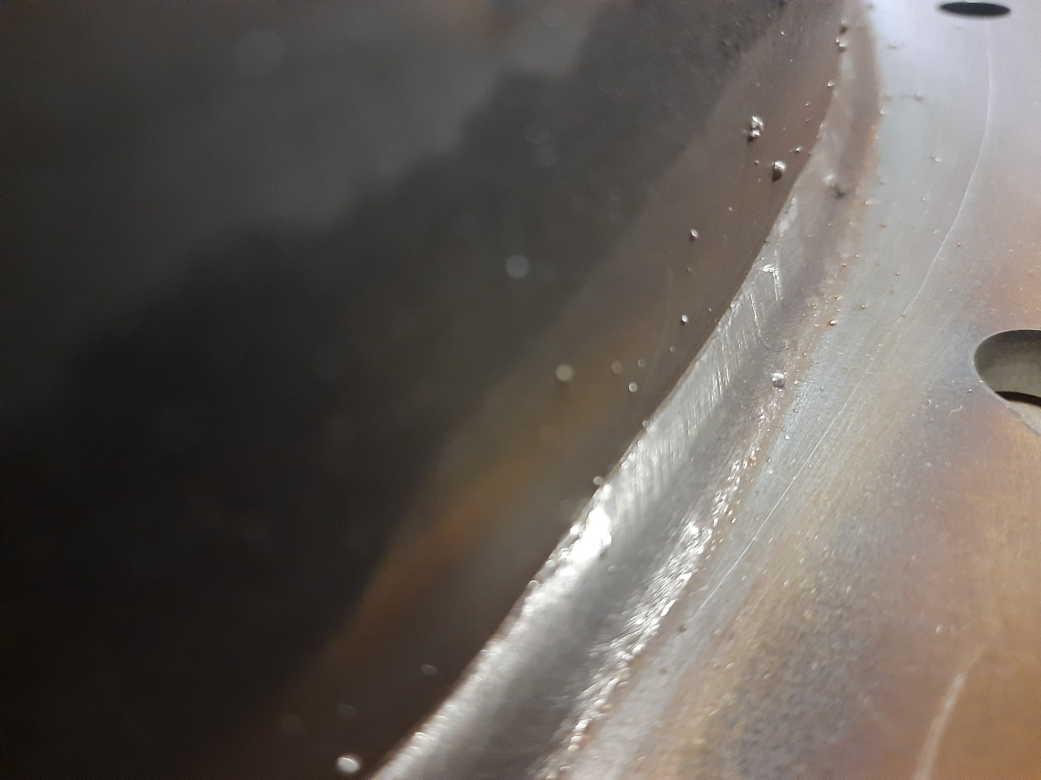 Zbliżenie na spoinę łączącą dwie metalowe powierzchnie, widoczne drobne krople i ślady obróbki.