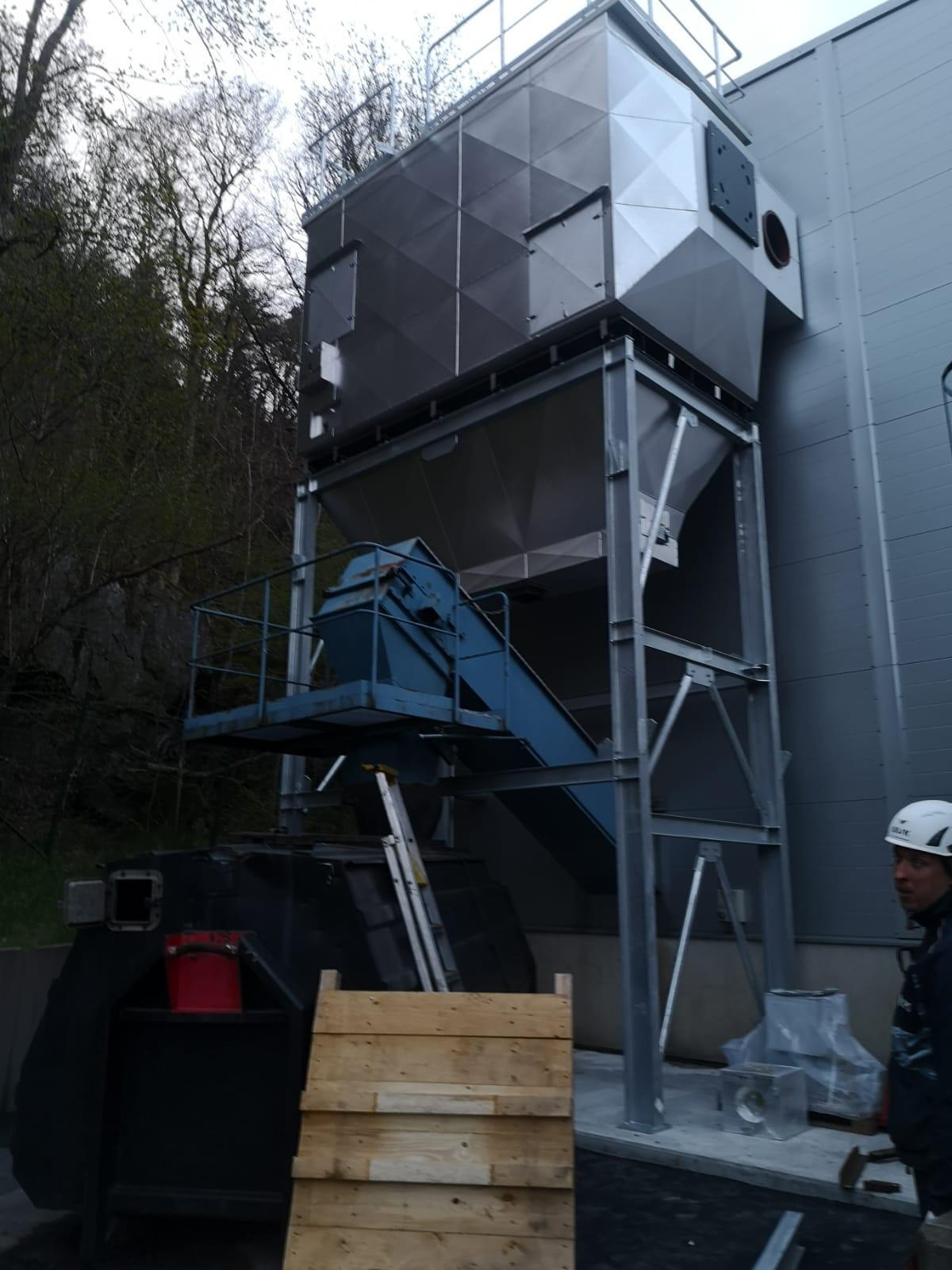 Metalowa konstrukcja przemysłowa z elementami transportującymi, widoczna drabina i pracownik w kasku.