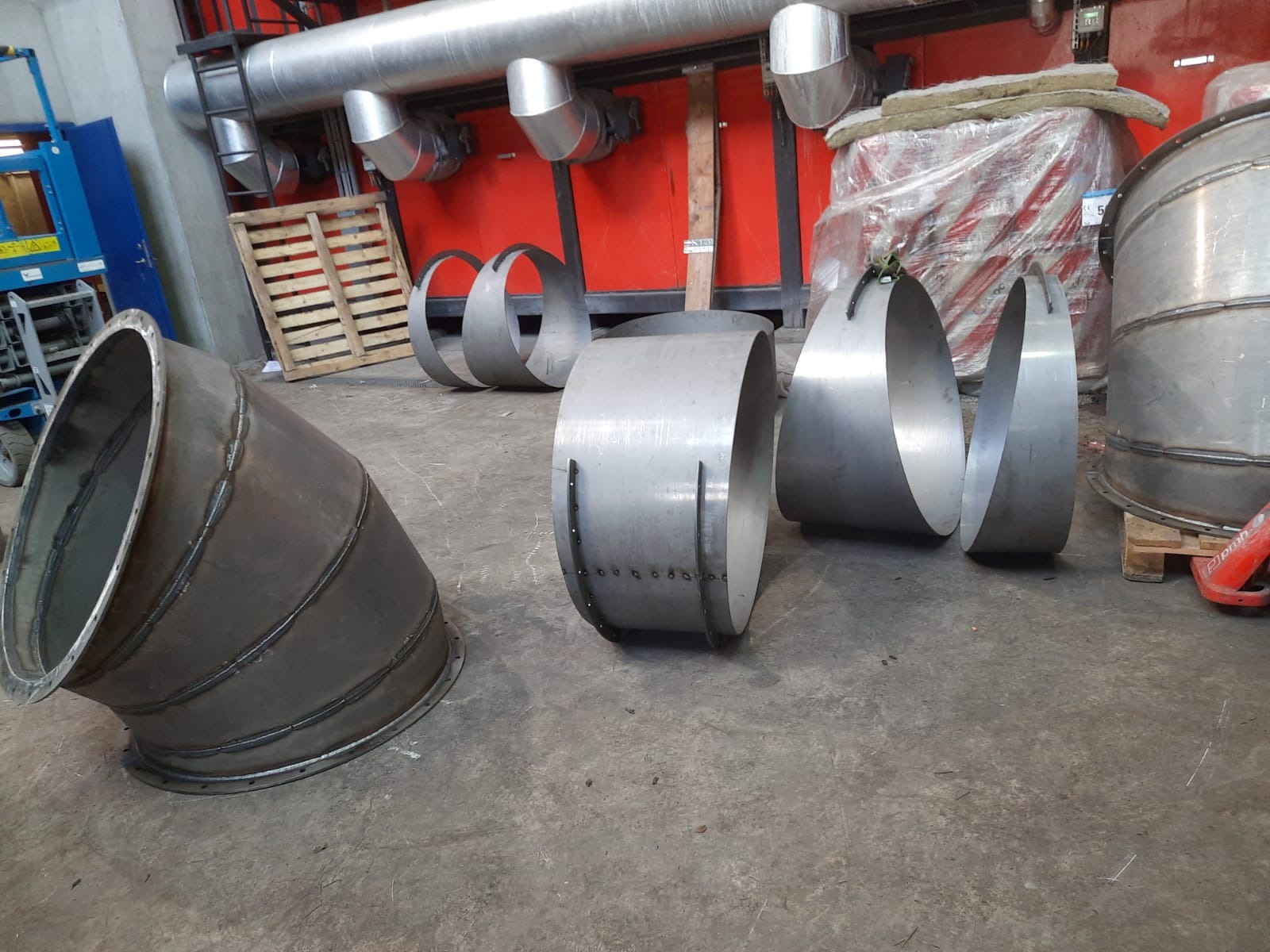 Elementy konstrukcji stalowej: spawane rury i segmenty rur z metalu, przygotowane do montażu w hali przemysłowej, widoczne ślady spawania i łączenia.