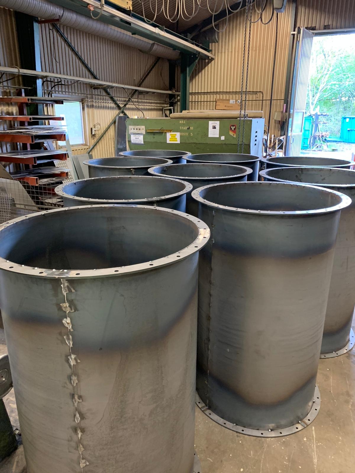 Metalowe cylindryczne elementy konstrukcyjne z widocznymi spawami i kołnierzami, ustawione w hali produkcyjnej.