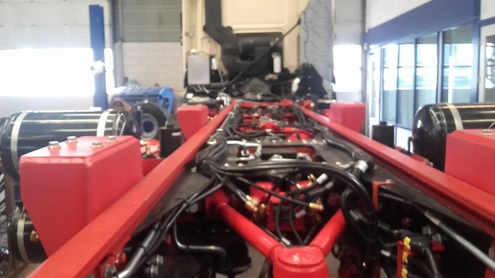 Czerwona rama podwozia ciężarówki z widocznymi zbiornikami powietrza i licznymi przewodami w warsztacie.