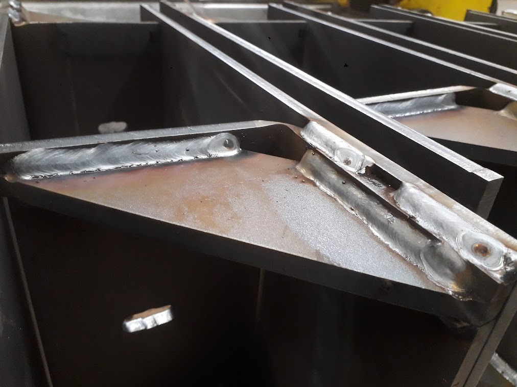 Spoina łącząca elementy konstrukcji stalowej, widoczne ślady spawania na metalu, detale łączeń kątowych.