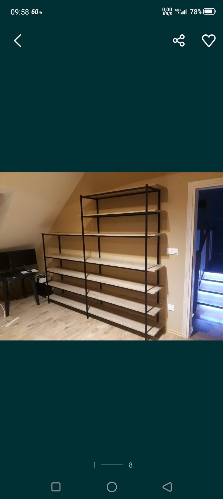 Regał z jasnego drewna i czarnych metalowych ram w pokoju. Widoczne schody z podświetleniem w tle. Minimalistyczny design.