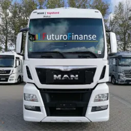 Biała ciężar&oacute;wka MAN widziana z przodu, z logo 'Futuro Finanse' na przedniej szybie, stojąca na placu z innymi ciężar&oacute;wkami w tle.