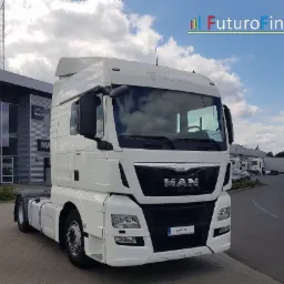 Biały ciągnik siodłowy MAN z widocznym logo Futuro Finanse w tle, zaparkowany na placu przed budynkiem dealera, z innymi pojazdami w tle.