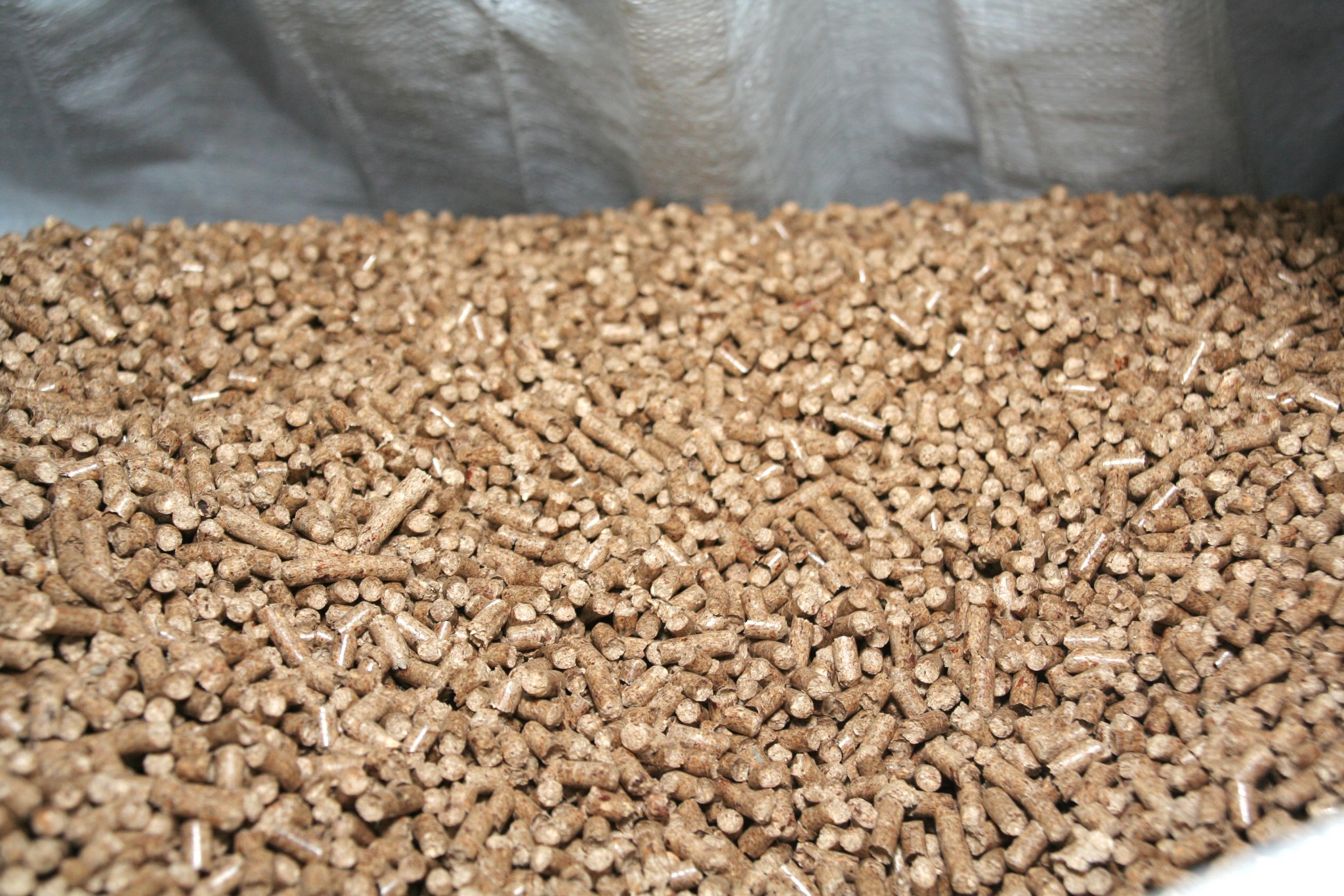 Jasnobrązowy pellet drzewny w worku, widoczne drobne fragmenty drewna w strukturze pelletu.