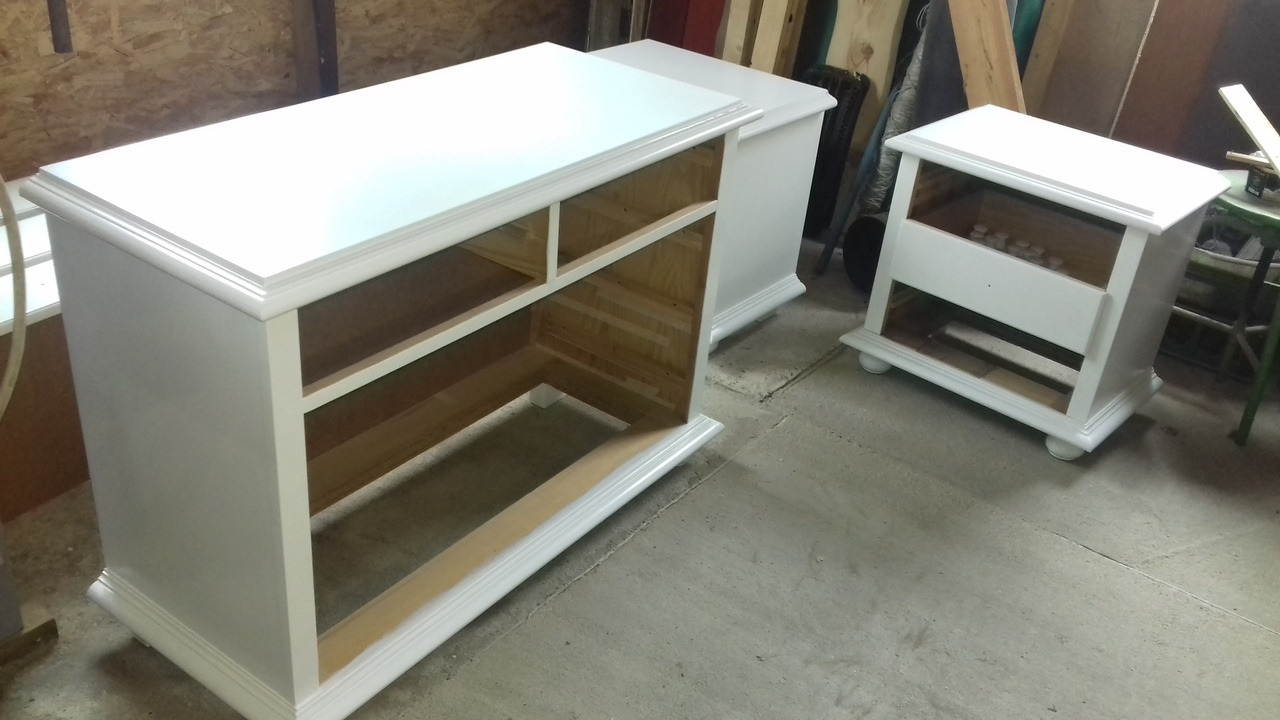 Białe, niedokończone szafki z otwartymi półkami w warsztacie, widoczne surowe drewno wewnątrz, detale dekoracyjne na krawędziach.