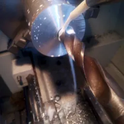 Wiertło podczas obróbki metalowego elementu na tokarce CNC, chłodziwo spływa na wióry.