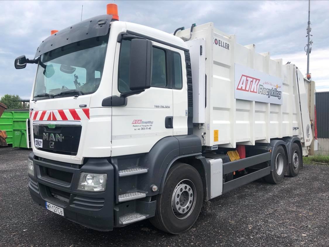 Biała śmieciarka MAN z czerwono-białymi pasami na przodzie i logo firmy ATK Recykling na boku, zaparkowana na żwirowym placu.
