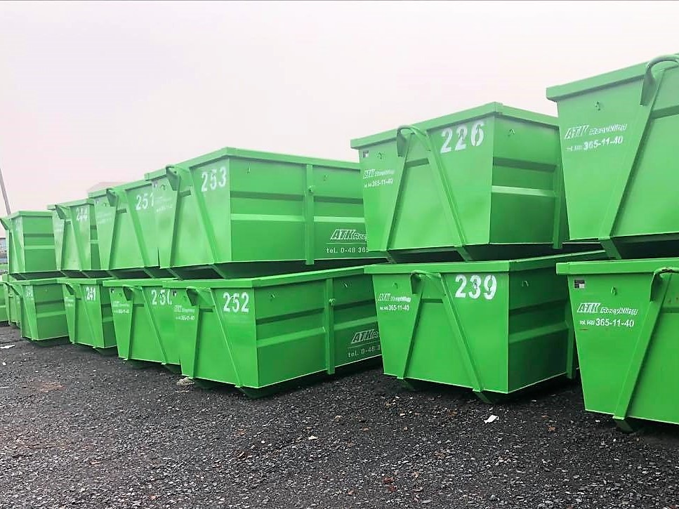Rząd świeżo pomalowanych na zielono kontenerów na gruz z numerami, ustawionych jeden na drugim na żwirowym podłożu, z widocznym logo firmy 'ATK Recycling' i numerem telefonu.