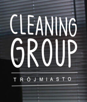 Biały napis 'CLEANING GROUP TRÓJMIASTO' na szklanej powierzchni, prawdopodobnie okno lub drzwi, z widocznymi żaluzjami w tle.