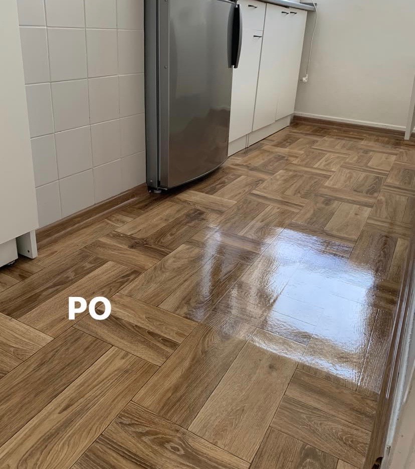 Błyszcząca, drewnopodobna podłoga ułożona w jodełkę w kuchni, widok po czyszczeniu lub renowacji, z widocznym napisem 'PO'.