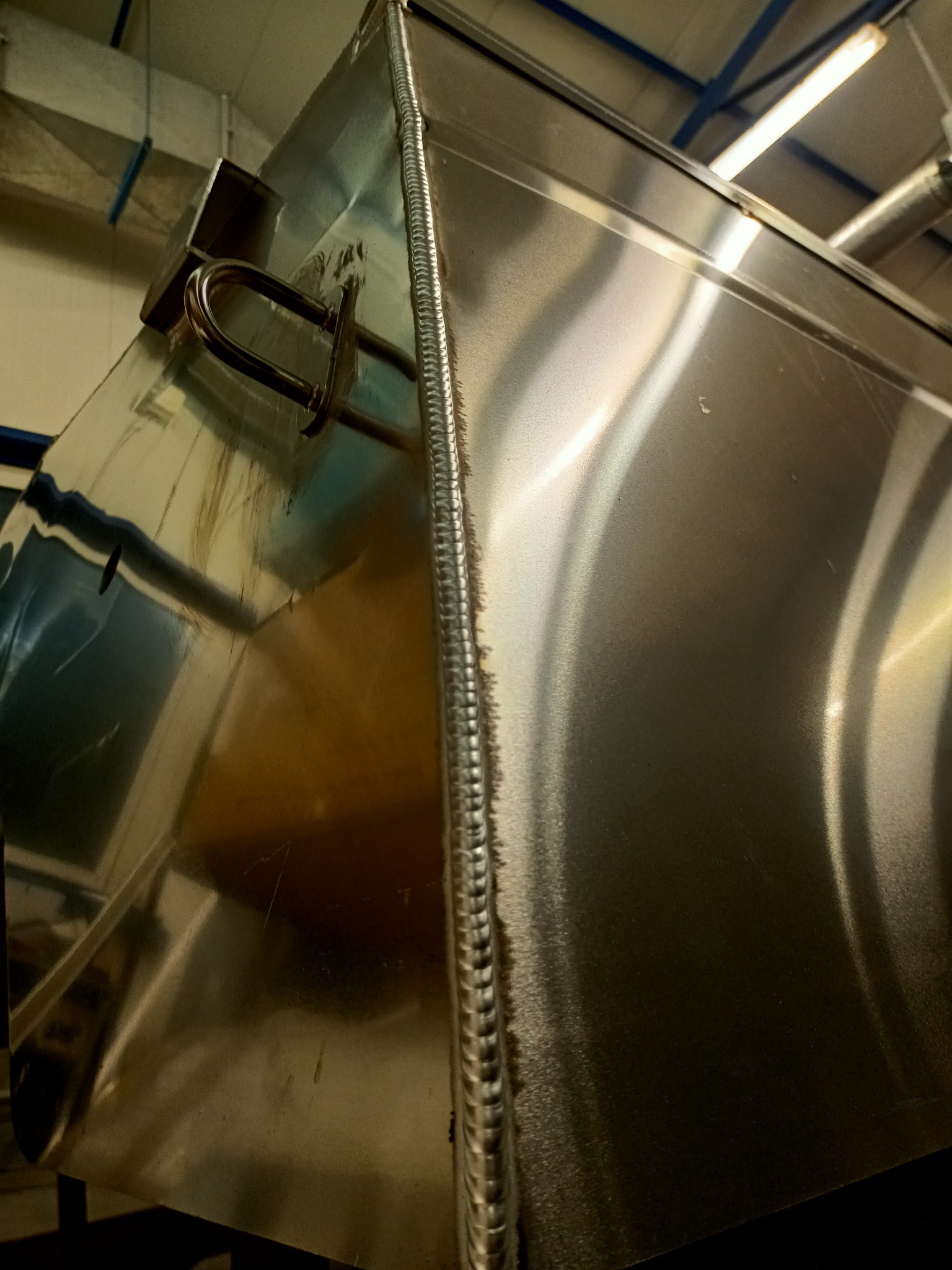 Metalowa konstrukcja zbiornika z widocznym spawem na krawędzi, uchwyt transportowy w górnej części, widok z dołu.