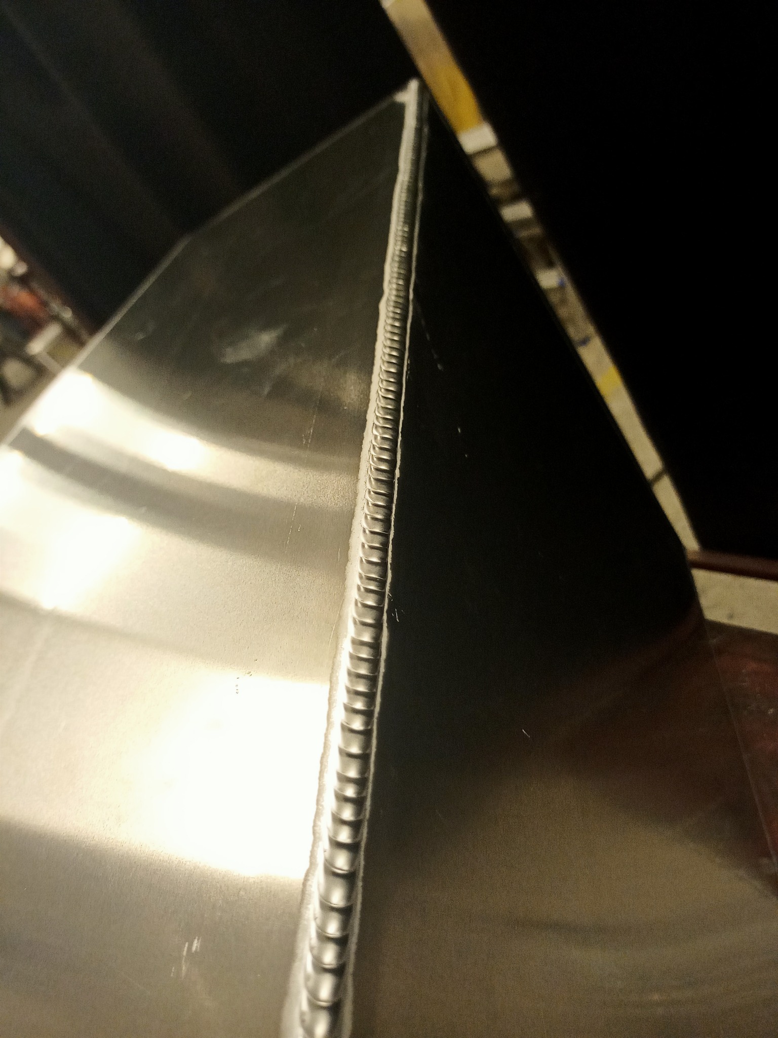 Szlif spoiny na metalowej powierzchni, widoczne regularne ślady po procesie łączenia.