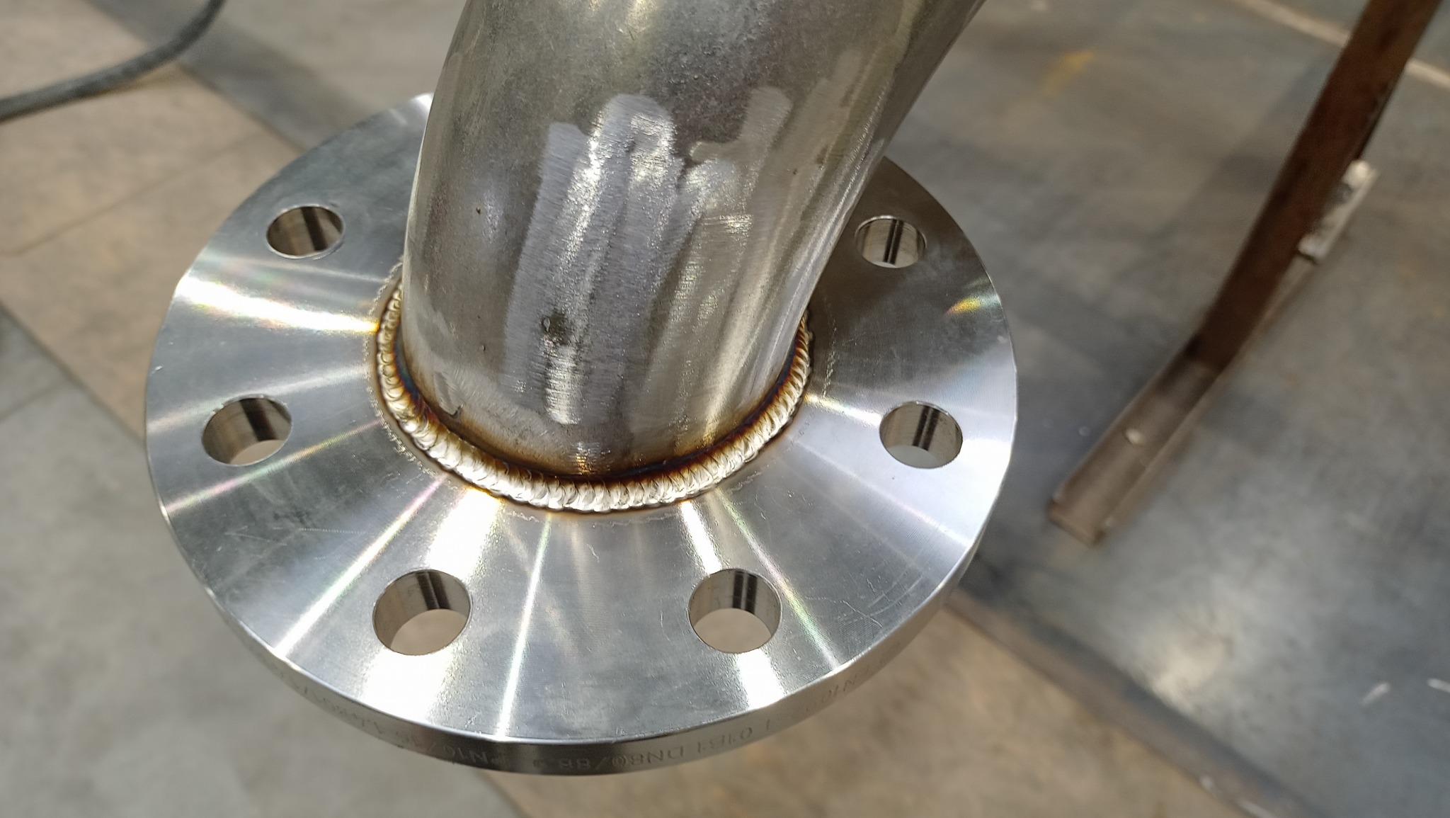 Połączenie spawane rury ze stali nierdzewnej z kołnierzem, widoczne ślady obróbki na powierzchni rury i spawu.