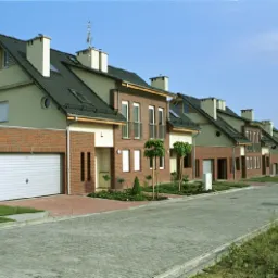 Szeregowiec z ceglaną fasadą i garażem, widok z perspektywy ulicy w słoneczny dzień.